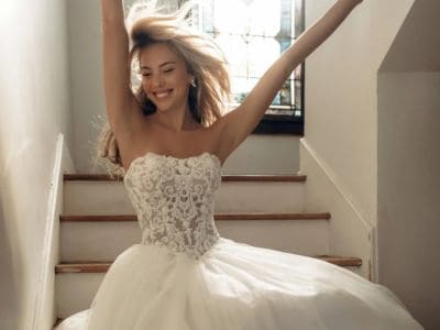 Junge Braut in weißem Hochzeitskleid auf Treppe mit Sonnenlicht.