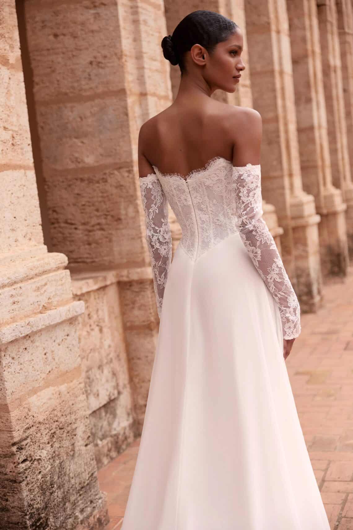 Elegantes Brautkleid mit Spitzenärmeln und offener Rücken vor historischen Säulen.