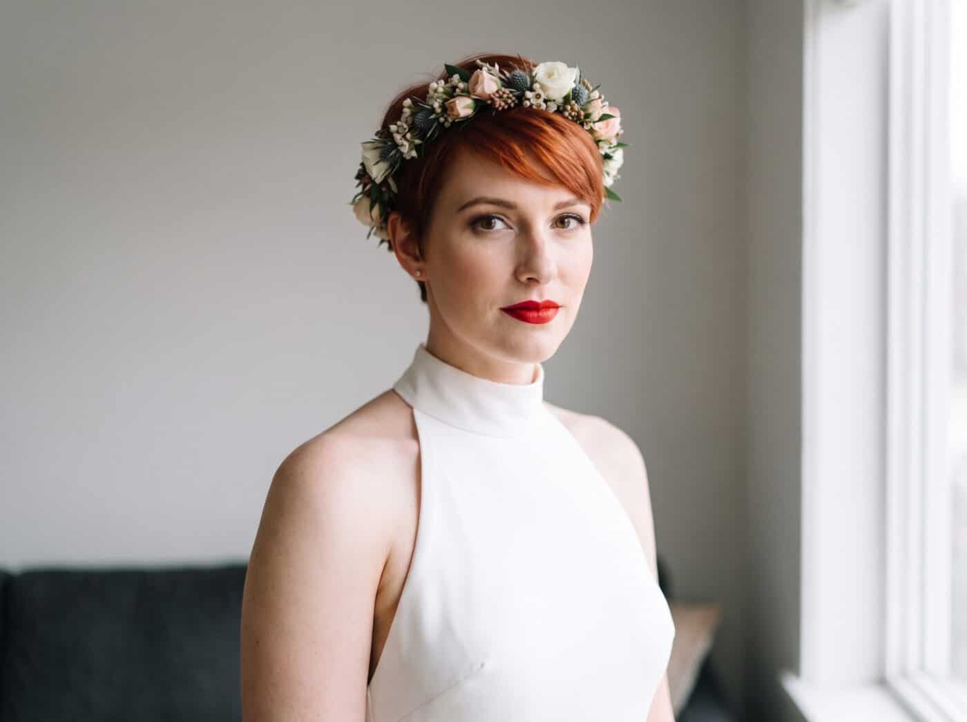 Braut mit rotem Kurzhaarschnitt und Blumenkranz bei Hochzeit.